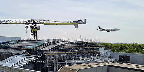 A photograph of an Emirates airbus a380 about to land at London Gatwick, with the Gatwick train station under construction in the foreground, with a large crane