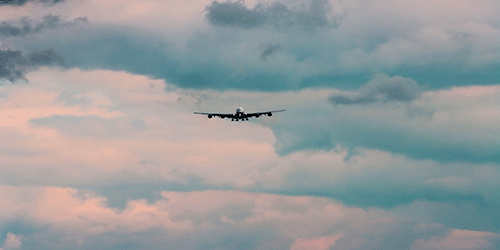 a long range photo of an a380 coming in to land amid peach coloured stormy sunset skies