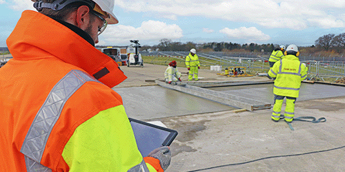 Photo of man in high vis jacket holding digital tablet supervising concrete pouring on the airfield