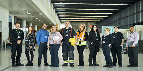 a group photo taken in the North Terminal of 9 Gatwick colleagues from various departments across the airport, such as IT, security, a Fire fighter and passenger assistance