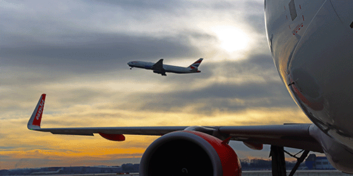 A cinematic photograph of a British airways Boeing 777 taking off in front of a colourful sunrise sky, with an easyJet airbus a320 parked in the foreground