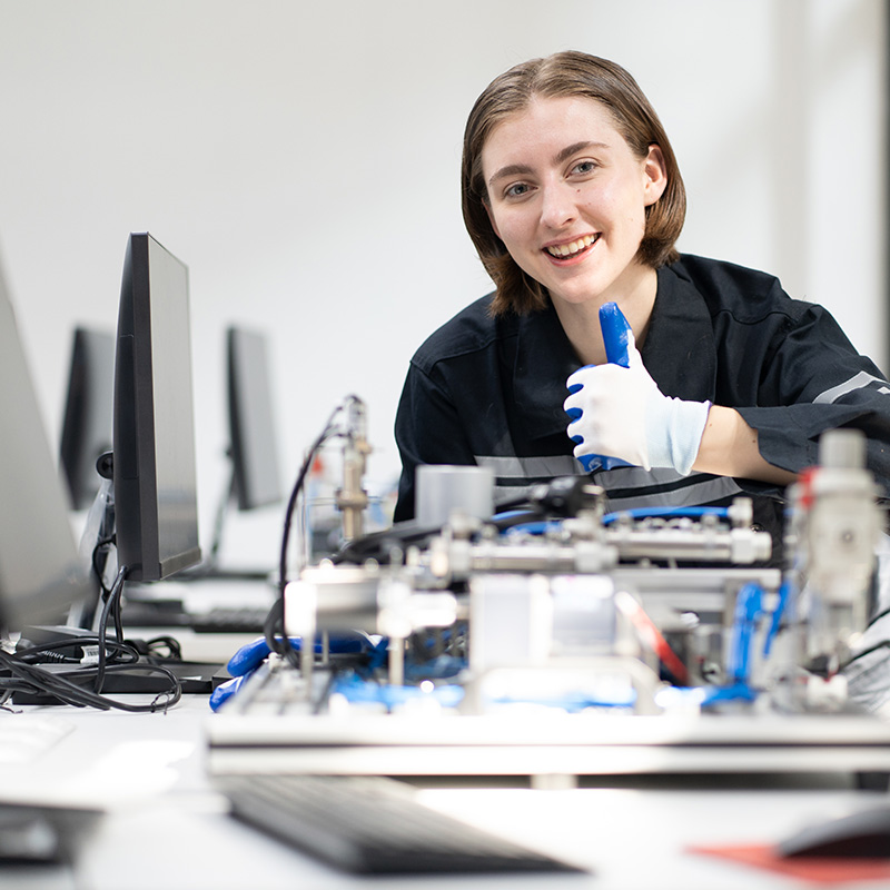 a photo of a young woman giving a thumbs up to the camera as they lean over a dismantled computer