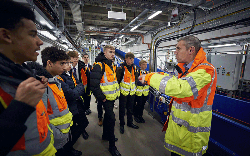 Several teenage students wearing high vis jackets stood in part of the baggage system facilities, with a Gatwick colleague showing them how it works
