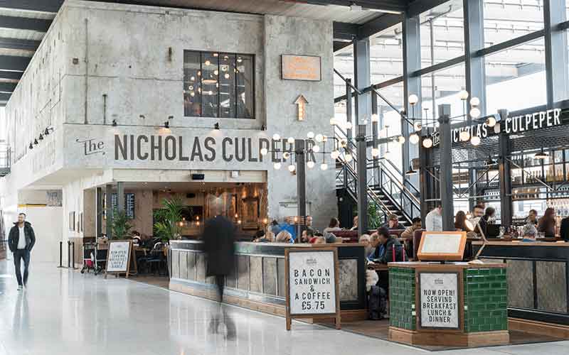 A long exposure photograph of The Nicholas Culpeper restaurant exterior in London Gatwick's North Terminal, with movement blurred passengers dining and walking past