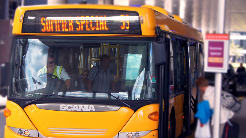A woman boarding a yellow Summer Special bus at Gatwick Airport - image is the work of Chris Sampson https://www.flickr.com/photos/lodekka/8278005275/in/photostream/ and has been used and altered with permission under the Creative Commons licence - https://creativecommons.org/licenses/by/2.0/