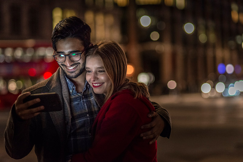 A young couple looking at their phones whilst on an evening out together