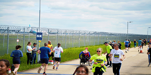 a photo of a charity marathon called Run Gatwick taking place net to the airfield boundary fence with planes on the runway visible in the background