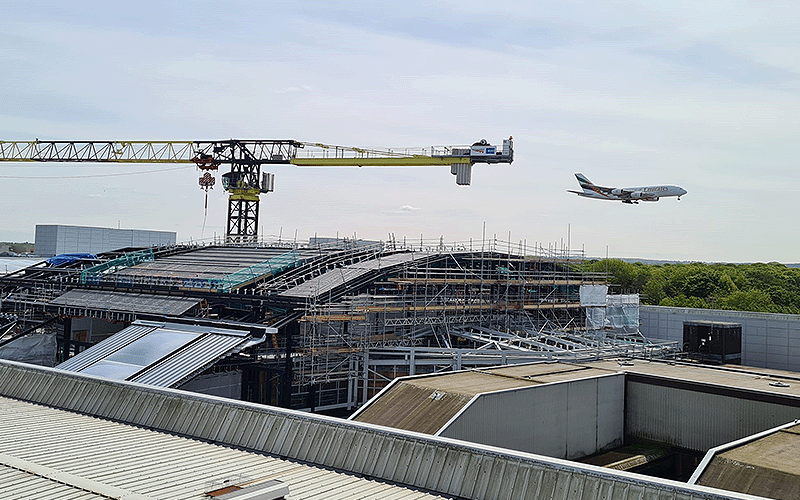 A photograph of an Emirates airbus a380 about to land at London Gatwick, with the Gatwick train station under construction in the foreground, with a large crane