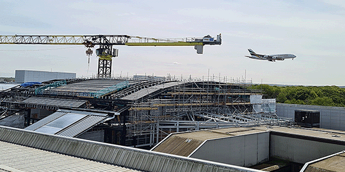 A photograph of an Emirates airbus a380 about to land at London Gatwick, with the Gatwick train station under construction in the foreground, with a large crane